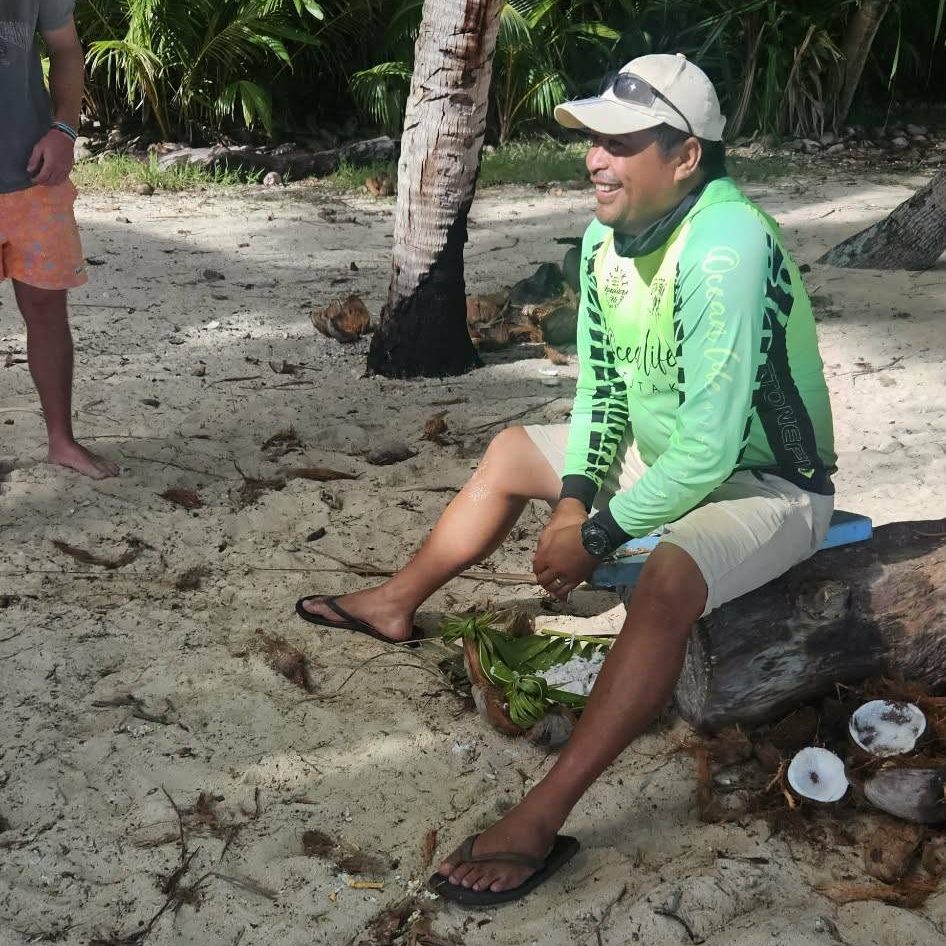 One of our crew grating coconut on the sand, with husked shells beside him