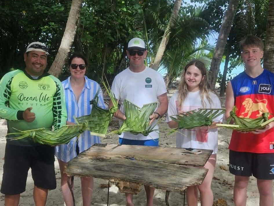 Guests on the sand holding plates they have just woven from coconut fronds